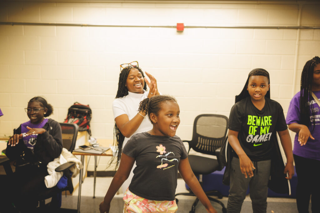 A child smiles in the middle of a classroom circle of other children and educators.