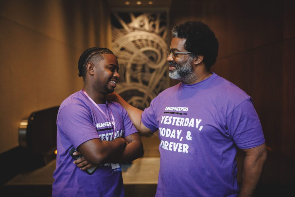 Sharif El-Mekki smiles and reaches out to a young person who is also smiling.